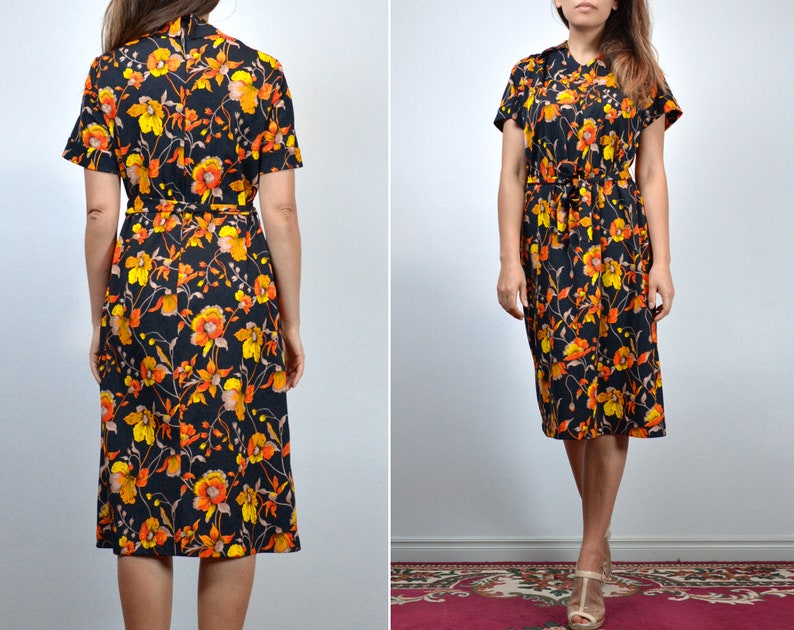 Puede incluir: Un vestido midi negro con estampado floral en tonos naranja, amarillo y marr&oacute;n. El vestido tiene manga corta y un lazo en la cintura.