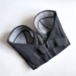 May include: A black bustier with a structured design, featuring a scalloped edge and intricate lace detailing. The interior is lined with a light gray fabric. The garment has adjustable closures and a classic silhouette.