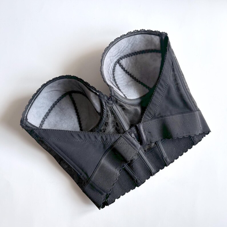 May include: A black bustier with a structured design, featuring a scalloped edge and intricate lace detailing. The interior is lined with a light gray fabric. The garment has adjustable closures and a classic silhouette.