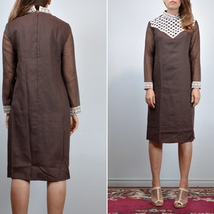 May include: A brown vintage dress with long sheer sleeves and a high collar. The collar and cuffs feature a white and brown geometric pattern. The dress has a knee-length hemline and a simple, elegant silhouette, perfect for a retro look.