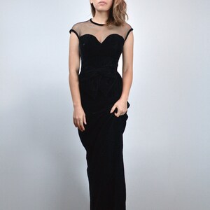 May include: A black velvet evening gown with a sheer neckline and cap sleeves. The bodice features a sweetheart neckline and a fitted waist, flowing into a floor-length skirt. The dress is a classic, elegant design.