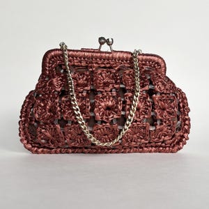 May include: A maroon crocheted clutch with a silver chain strap. The bag features a kiss-lock clasp and a woven pattern. The chain is silver and the bag is a solid maroon color.