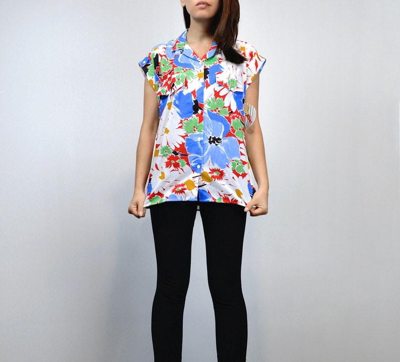 May include: A short-sleeved button-down shirt with a vibrant floral pattern. The shirt features large blue, red, and green flowers on a white background. The shirt is paired with black leggings.