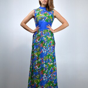 May include: A long, sleeveless dress with a high neck. The dress is patterned with a colourful floral design in blue, green, and red. A solid blue band defines the waist. The fabric looks lightweight, ideal for warmer temperatures. The dress is a vintage style.