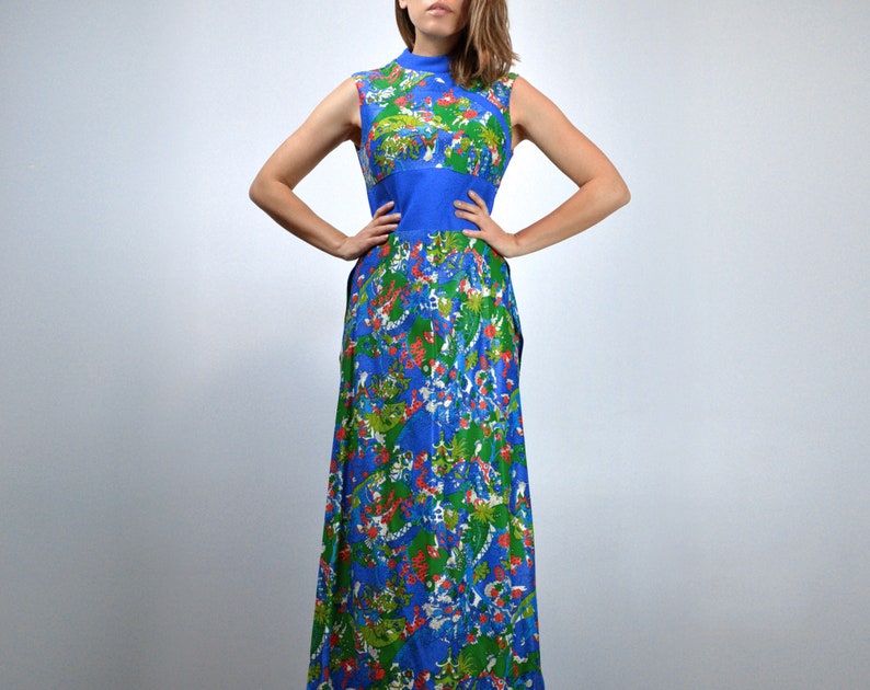 May include: A long, sleeveless dress with a high neck. The dress is patterned with a colourful floral design in blue, green, and red. A solid blue band defines the waist. The fabric looks lightweight, ideal for warmer temperatures. The dress is a vintage style.