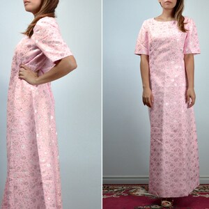 May include: A light pink, floor-length dress with short sleeves. The dress features a subtle floral pattern in a lighter shade of pink and silver. The dress has a round neckline and a straight silhouette, suitable for formal occasions.