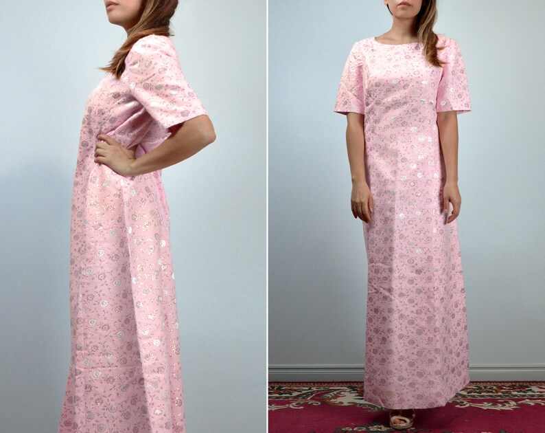 May include: A light pink, floor-length dress with short sleeves. The dress features a subtle floral pattern in a lighter shade of pink and silver. The dress has a round neckline and a straight silhouette, suitable for formal occasions.