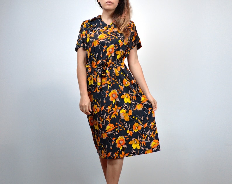 Puede incluir: Un vestido midi negro con estampado floral con flores naranjas y amarillas. El vestido tiene manga corta y un lazo en la cintura.
