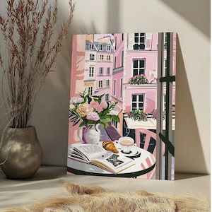 Peut inclure: Une peinture repr&eacute;sentant une sc&egrave;ne de caf&eacute; parisien avec un b&acirc;timent rose, une table avec un livre, un croissant et une tasse de caf&eacute;. Le caf&eacute; est situ&eacute; dans une rue avec d'autres b&acirc;timents en arri&egrave;re-plan. La peinture est encadr&eacute;e et a un passe-partout blanc.