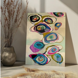 May include: Abstract art print featuring colorful, organic shapes in shades of blue, pink, green, and black against a cream background. The artwork has a modern aesthetic, with a layered, watercolor-like effect. The canvas is displayed near a vase with dried plants.