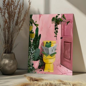 May include: A rectangular wall art print featuring a green frog sitting on a yellow toilet reading a newspaper. The scene is set in a room with pink walls, a pink door, and various green potted plants including a tall cactus and a hanging vine.