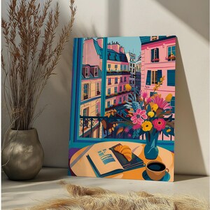 Peut inclure: Une peinture color&eacute;e d'une sc&egrave;ne de rue parisienne avec une vue sur les b&acirc;timents et un balcon. Un bouquet de fleurs dans un vase bleu est pos&eacute; sur une table avec un livre et une tasse de caf&eacute;.