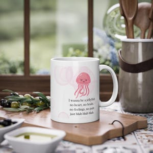 Könnte beinhalten: Eine weiße Keramiktasse mit einer rosa Quallen-Illustration und dem Text "I wanna be a jellyfish no heart, no brain. no feelings, no pain just blub blub blub."