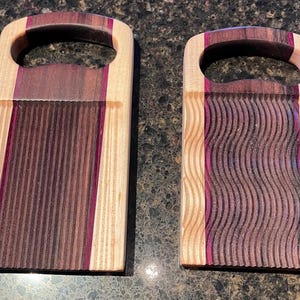 May include: Two rectangular wooden boards featuring integrated handles at the top. The boards are constructed from light-colored wood with dark brown and purple wood accents. One board has vertical grooves, while the other has wavy grooves.