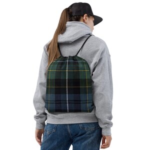 May include: A drawstring backpack with a green, blue, black, and yellow plaid pattern. The bag has black drawstrings and is worn over the shoulders. The bag is made of a durable fabric.