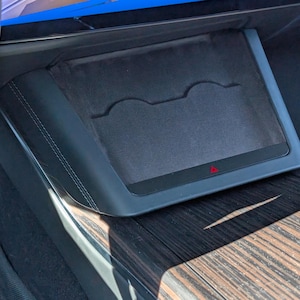 May include: A black car console with a dark gray, felt-lined storage compartment. The compartment has two curved cutouts and a small red triangle indicator. The console is set in a wood-grain panel.
