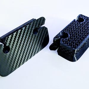 May include: Two black plastic 3D printed objects with a textured surface. One object has a more rounded shape and the other is more angular.