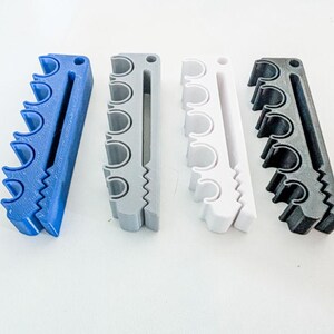 May include: Four rectangular organizers arranged in a row, each featuring five circular cutouts along one side and a long vertical slot. The organizers are colored blue, gray, white, and black, and each includes a small circular hole at the top.