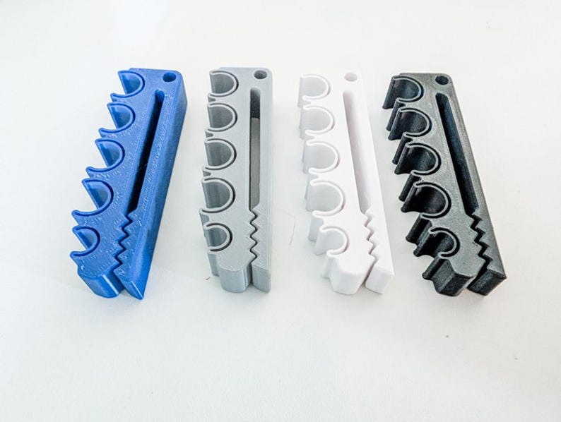 May include: Four rectangular organizers arranged in a row, each featuring five circular cutouts along one side and a long vertical slot. The organizers are colored blue, gray, white, and black, and each includes a small circular hole at the top.