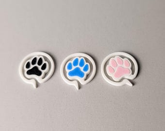 May include: Three white paw print-shaped speech bubbles. Each bubble contains a paw print in a different color: black, blue, and pink. The paw prints are centered within the white speech bubble outlines.