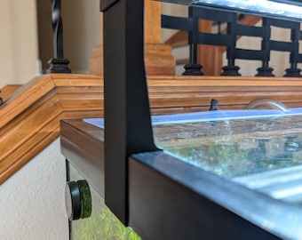 May include: Black aquarium light fixture mounted on a glass tank. The fixture has a rectangular LED light and a black metal frame. The tank has a green background with aquatic plants. A black control knob is visible on the side of the tank.