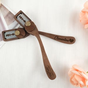 May include: Two wooden straight razors with exposed blades and brass fittings. One razor is engraved with the name "Clementine" and a heart. The other razor is engraved with text and a logo. The razors are made of dark wood.