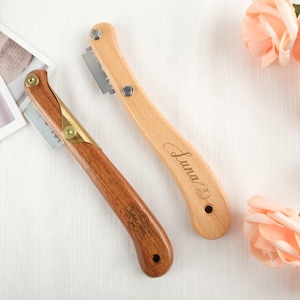 Puede incluir: Dos cuchillas para pan de madera. Una es de color claro con el nombre "Luna" grabado, y la otra es de madera oscura con un logotipo. Ambas tienen una cuchilla de metal y herrajes de latón o plata.