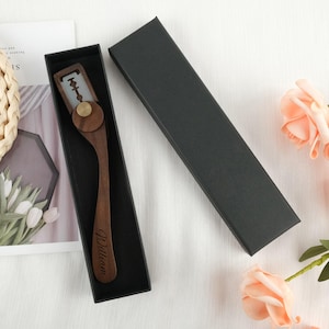 Op de afbeelding: Een houten straight razor met een metalen mes en een messing accent, gepresenteerd in een zwarte geschenkverpakking. De handgreep is gegraveerd met de naam "William". De razor wordt gepresenteerd op een wit oppervlak met bloemaccenten.