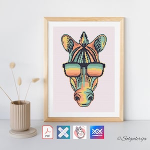 Puede incluir: Una obra de arte en punto de cruz enmarcada que representa la cabeza de una cebra colorida con gafas de sol. La cebra está representada en un estilo pixelado con un arcoíris de colores. La obra de arte está en un marco de madera.