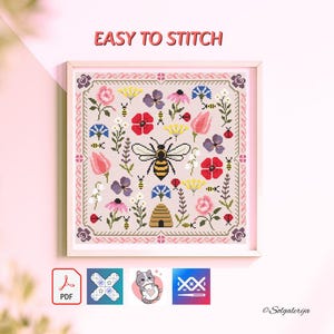 May include: A framed cross-stitch pattern featuring a bee, flowers, and a beehive. The design includes red, pink, yellow, blue, and purple flowers, with the text "EASY TO STITCH" at the top. The frame is white.