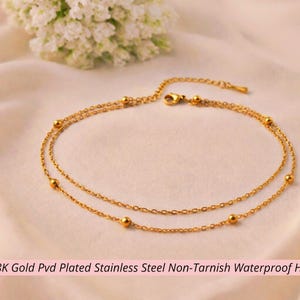 May include: A gold-colored, double-layered anklet with small, round beads. The anklet is made of stainless steel and is hypoallergenic. The image also includes text that reads "18K Gold Pvd Plated Stainless Steel Non-Tarnish Waterproof Hypoallergenic."