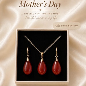 K&ouml;nnte beinhalten: Ein goldfarbenes Halsketten- und Ohrring-Set mit tropfenf&ouml;rmigen, rot-orangen Anh&auml;ngern, pr&auml;sentiert in einer Geschenkbox. Der Text "Mother's Day" und "A special gift for the most beautiful woman in my life" sind im Bild zu sehen.