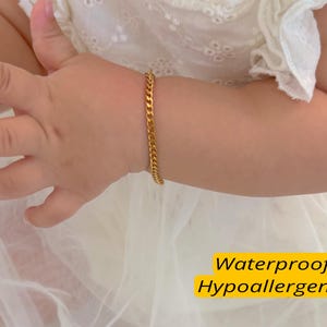 Pode incluir: Uma pulseira de corrente dourada é usada no pulso de uma criança. A pulseira é feita de pequenas elos interligados. A imagem inclui o texto "Waterproof" e "Hypoallergenic" em uma caixa amarela.
