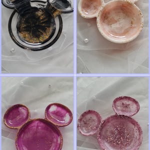 Pu&ograve; includere: Quattro piatti decorativi in resina a forma di orecchie di Topolino. I piatti sono in vari colori, tra cui nero con glitter dorati, rosa con glitter dorati e magenta con glitter dorati. I piatti sono su una superficie bianca.