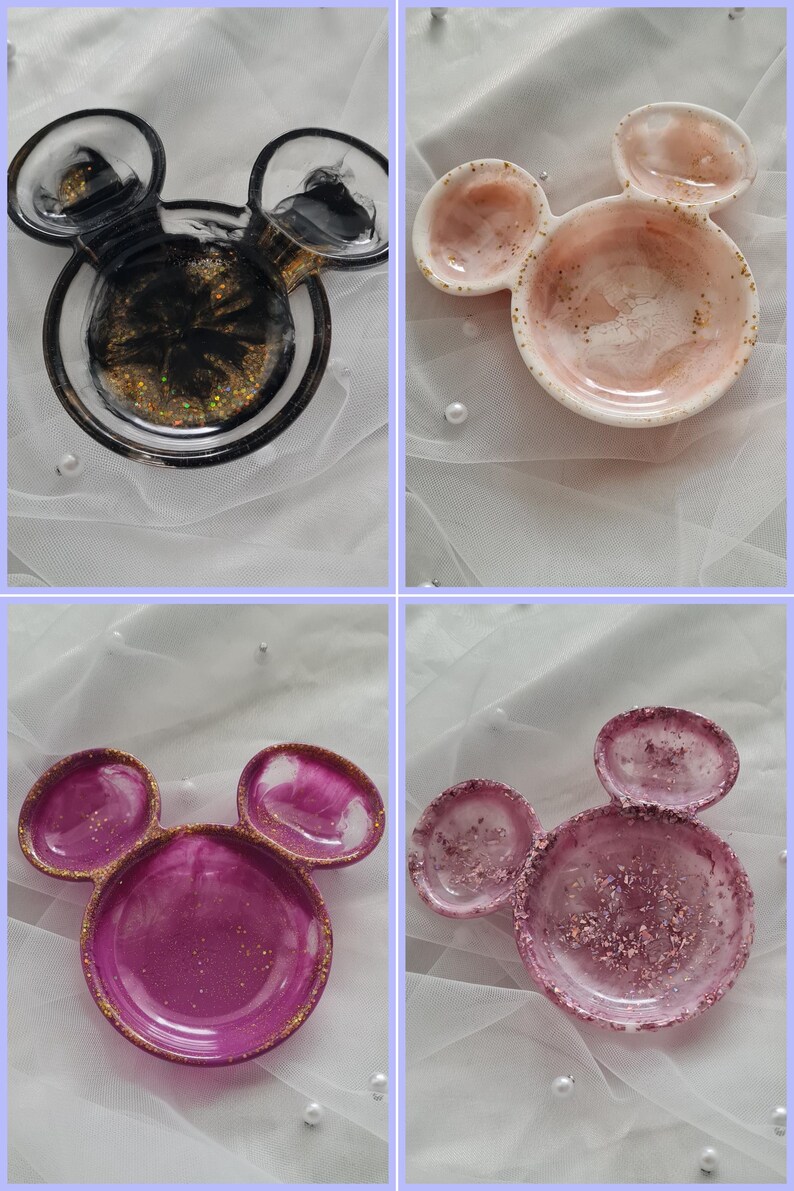 Pu&ograve; includere: Quattro piatti decorativi in resina a forma di orecchie di Topolino. I piatti sono in vari colori, tra cui nero con glitter dorati, rosa con glitter dorati e magenta con glitter dorati. I piatti sono su una superficie bianca.