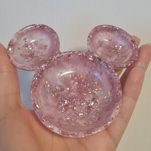 Pu&ograve; includere: Un piatto in resina rosa a forma di testa di Topolino. Il piatto &egrave; riempito di glitter e ha una finitura lucida. Le orecchie sono piatti pi&ugrave; piccoli e arrotondati. &Egrave; un oggetto decorativo.