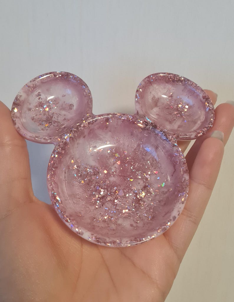 Pu&ograve; includere: Un piatto in resina rosa a forma di testa di Topolino. Il piatto &egrave; riempito di glitter e ha una finitura lucida. Le orecchie sono piatti pi&ugrave; piccoli e arrotondati. &Egrave; un oggetto decorativo.