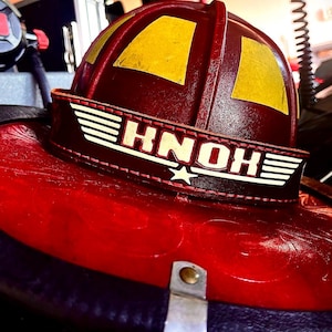 Könnte beinhalten: Ein roter Feuerwehrhelm mit gelben Akzenten und dem Schriftzug "HNOH" auf einem Lederband. Der Helm hat einen breiten Rand und ein Sternemblem, was auf seinen Einsatz im Notdienst hindeutet. Er ist wahrscheinlich robust.