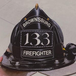 May include: A black firefighter helmet with the text "BROWNSBURG" and the number "133" in white. The word "FIREFIGHTER" is also displayed. A small light is attached to the side of the helmet.