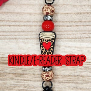May include: A beaded strap featuring a central coffee cup charm with a leopard print and red heart design. The strap includes two beige beads with brown coffee-themed patterns, two silver rhinestone spacers, and one solid red bead, finished with black metal clasps.