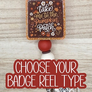 May include: A square badge reel featuring a brown background with white text that reads take me to the Pumpkin Patch, surrounded by orange and white floral and pumpkin illustrations. The reel has a glittery border and a red and white bead accent.