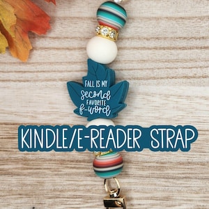 May include: A beaded strap featuring a teal leaf-shaped charm with the text 'FALL IS MY second FAVORITE f-word'. The strap includes striped teal, white, and metallic gold-toned beads, finished with gold-toned metal lobster clasps at both ends.