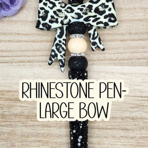 May include: A black rhinestone pen with a large bow. The bow features a black and white animal print. The pen has a black barrel covered in rhinestones and a black tip. The text on the image reads "RHINESTONE PEN - LARGE BOW."