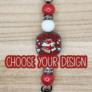 May include: A keychain with a black clasp and a series of beads. The design includes red glitter beads, a white bead, and a square charm with the text "BOOKS ARE MY LANGUAGE" and a stack of books. The text "CHOOSE YOUR DESIGN" is also present.
