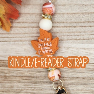 May include: A beaded strap featuring a gold-tone lobster clasp, marbled orange and white beads, a gold rhinestone spacer, and a central orange maple leaf charm with the white text 'FALL IS MY second FAVORITE f-word' printed on the surface.