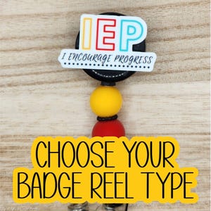 May include: A black badge reel featuring a white acrylic topper with the colorful text IEP and the phrase I ENCOURAGE PROGRESS. Below the topper are two round silicone beads in yellow and red, followed by a clear plastic strap clip.