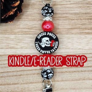 May include: A beaded strap featuring a central round black charm with a white skull graphic and the text HOCUS POCUS I NEED COFFEE TO FOCUS. The design includes black skull-patterned beads, red glitter beads, and silver-toned metal clasps.