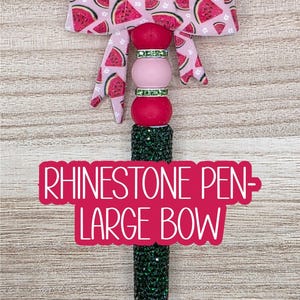 May include: A rhinestone pen with a large bow. The pen features a green, glittery barrel and a decorative top with pink beads and a watermelon-patterned bow. The text "RHINESTONE PEN - LARGE BOW" is displayed.