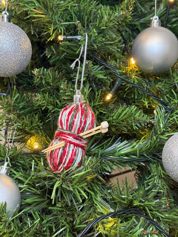 A perfectly miniaturized skein of wool with tiny knitting needles, hand-sculpted as a Christmas ornament — an instant inside-joke gift for any crafter.