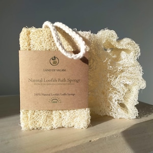 Puede incluir: Una esponja de baño de luffa natural con una etiqueta de papel marrón que dice "LAND OF SALAM Esponja de baño de luffa natural 100% esponja de luffa/luffa natural".